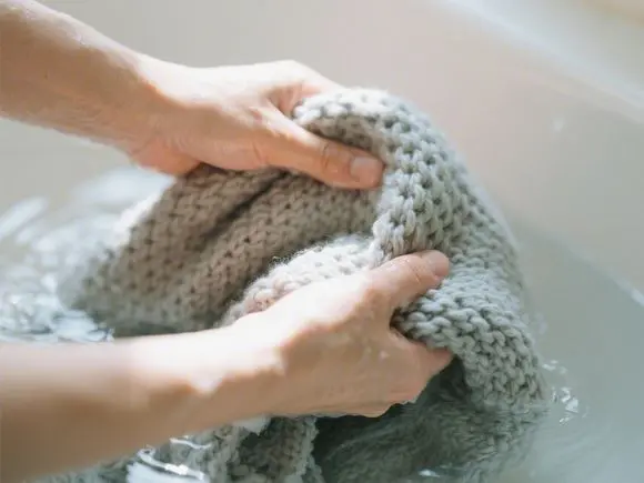 Soft-lighting-close-up-of-hands-gently-washing-a-knitted-throw-in-water